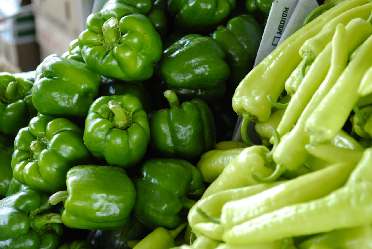 heros-img Close-up of fresh green bell peppers and chili peppers, showcasing vibrant and organic produce in a market setting.