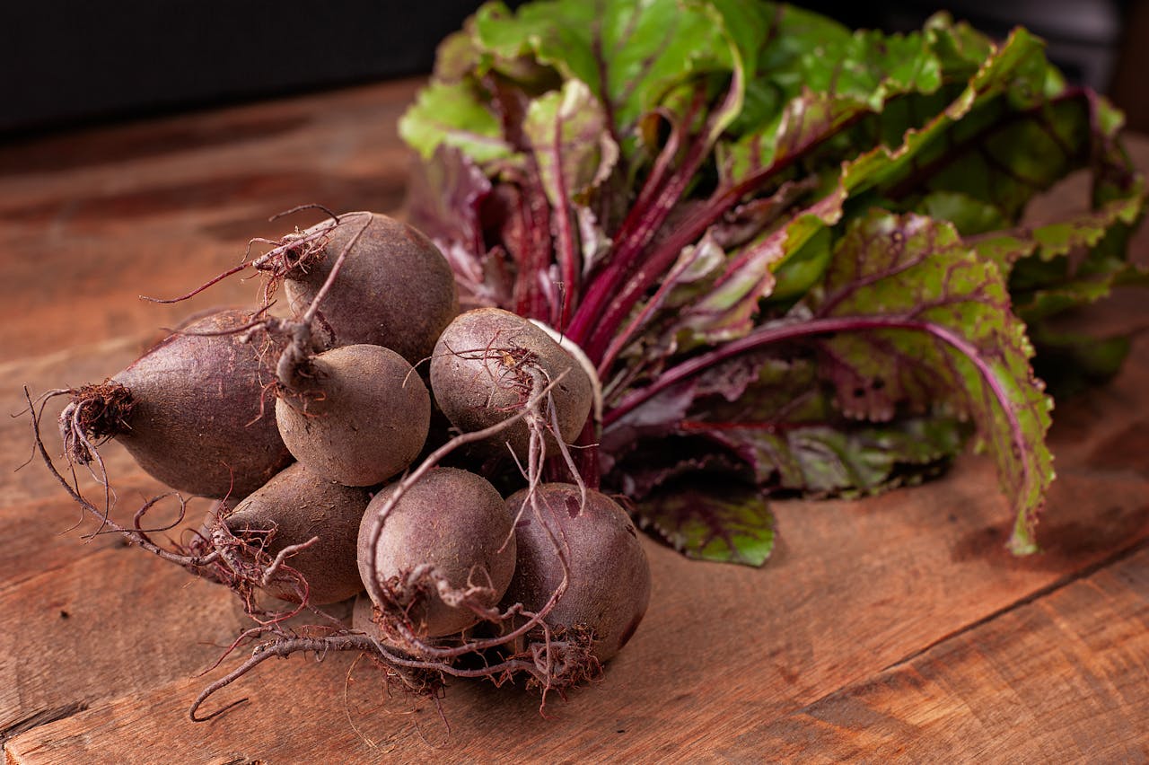 Bundle of fresh organic beetroots with vibrant green leaves on a wooden surface.
